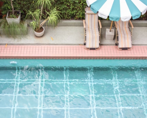 Piscina azul com duas espreguiçadeiras e um guarda sol.