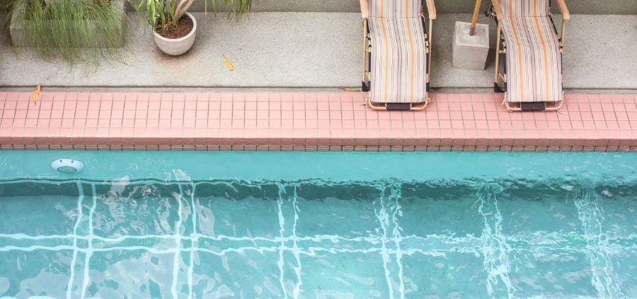 Piscina azul com duas espreguiçadeiras e um guarda sol.